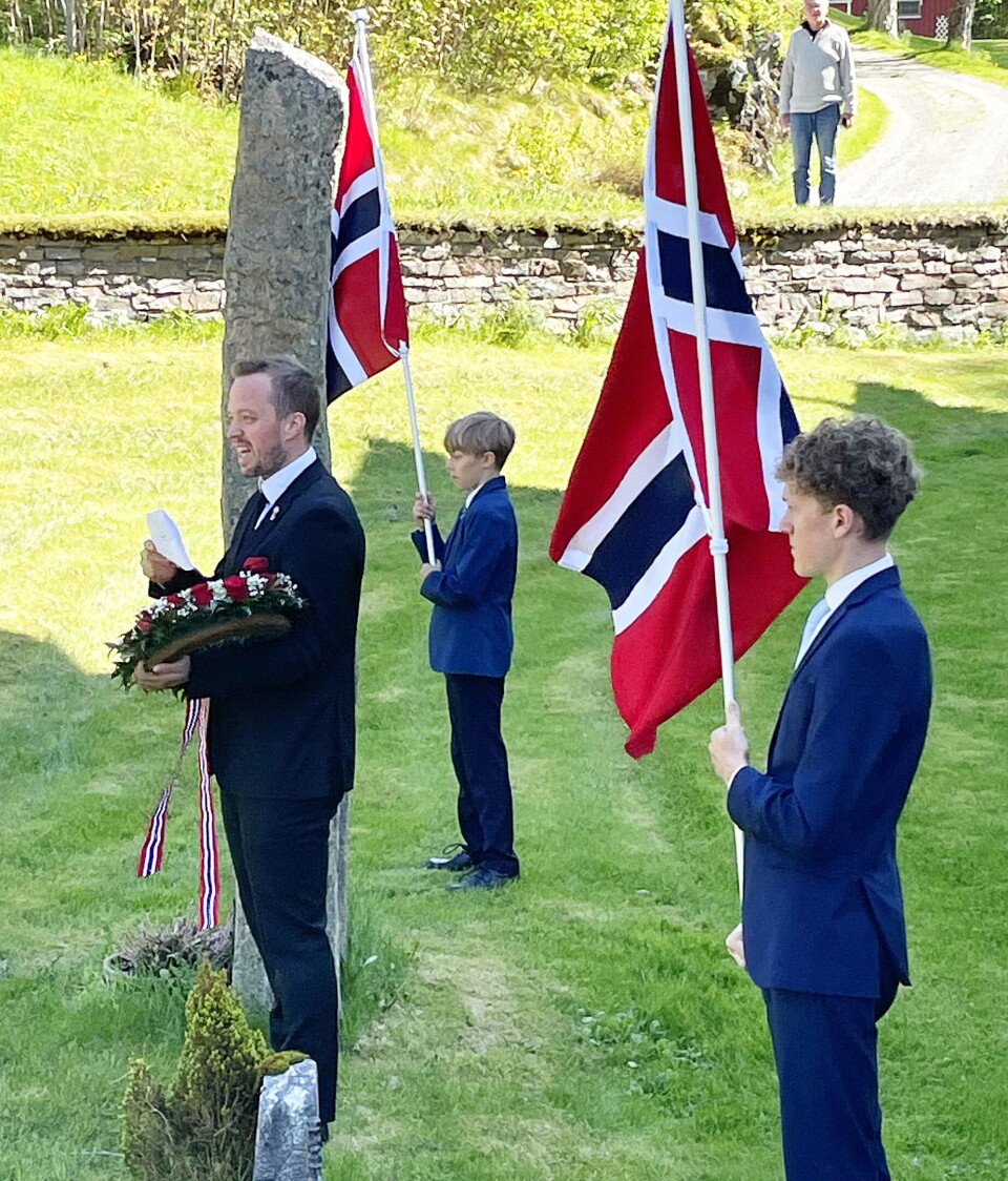 Sondre Bøe hadde ein flott appell ved soldatbautaen. Med flagga står Aasbø-brørne Harald og Vegard (nærast). mann og to gutter i dress med stort norsk flagg ved soldatbauta.