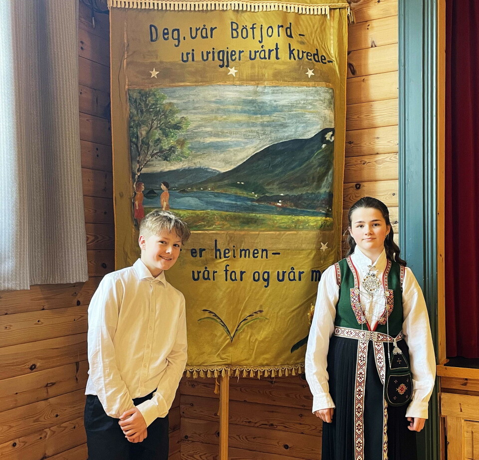 Konfirmantane Syver og Emilie attmed Bøfjord-fana etter å ha framført sin gode 17. mai-tale. gutt med skjorte og jente i bunad foran fane bilde og tekst om bøfjorden