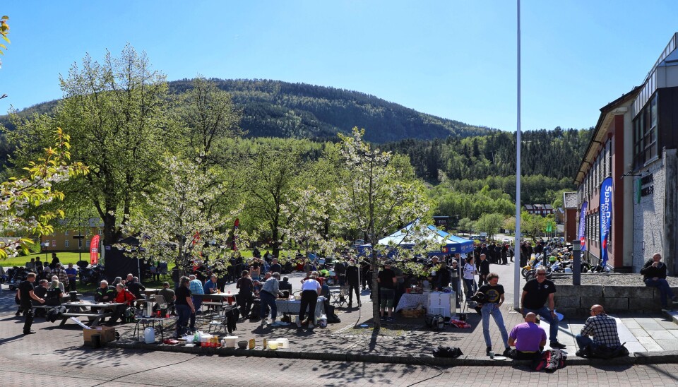 Surnadal viste seg fra sin beste side på Motorsykkelens dag i 2025. Avstandsbilde med utendørs sittegrupper, arrangør-kjøkken, parytelt m kaffe og bakels i forgrunnen. Parkeringsplassen i bakgrunnen. Blomstrende prydkirsebærtre og lysegrønne bjørker innimellom.