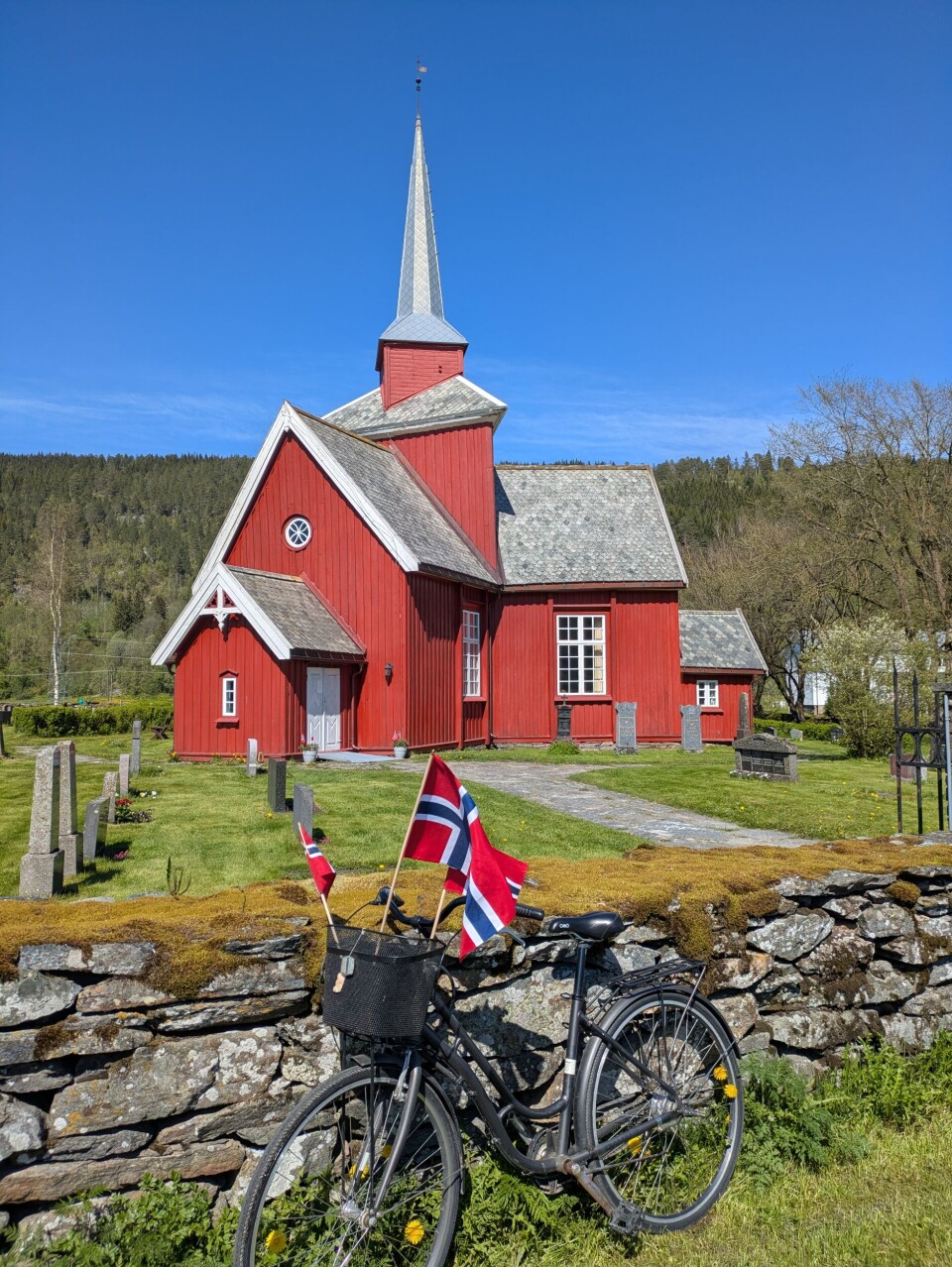 Fleire hadde parkert ved Mo kyrkje der eit langt tog med flott korps i spissen gjekk frå etter gudstenesta. Sykkel med norske flagg foran rødmalt kirke