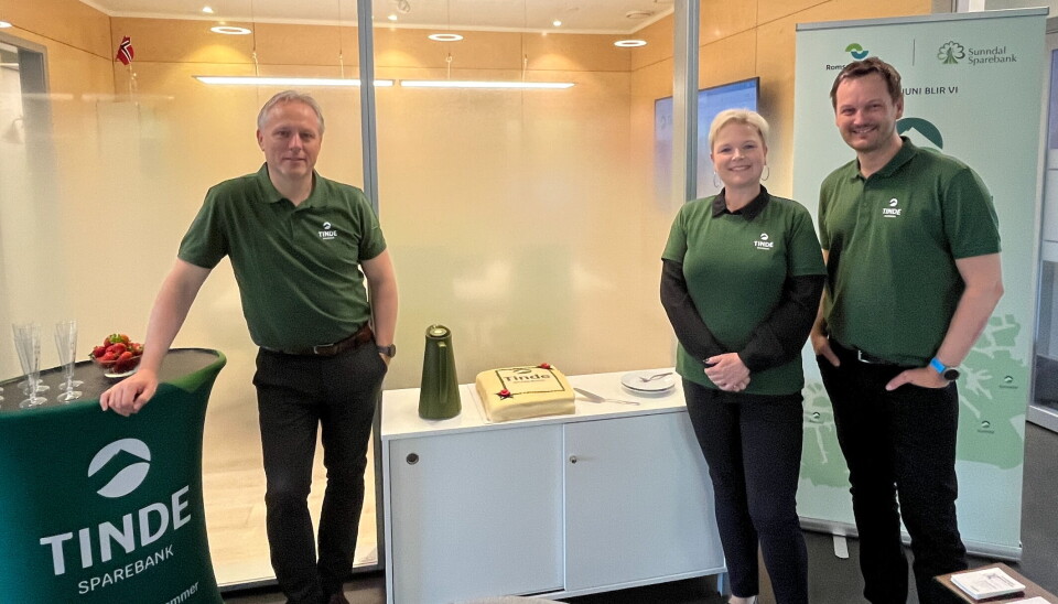 Leder forsikring Steinar Aasbø, avdelingsbanksjef Mette Helen Strand Mikkelsen og forsikringsrådgiver Torgrim Aaram Schaanning kan friste med sprudlende drikke og jordbær, kaffe og marsipankake på dagen for markering av sammenslåingen. Tre personer i like t-skjorter, oppstilt ved et bord med bløtkake.
