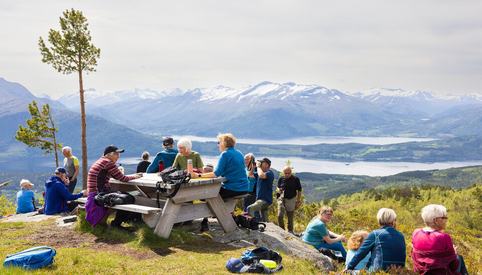 God og lang matpause på Klåberget. Noen mennesker sitter på en benk, andre på gresset. Fin naturutsikt.
