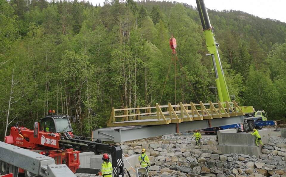 Mannskapene styrer konstruksjonen på plass. Kran, bru og arbeidarar i gule arbeidsklede.
