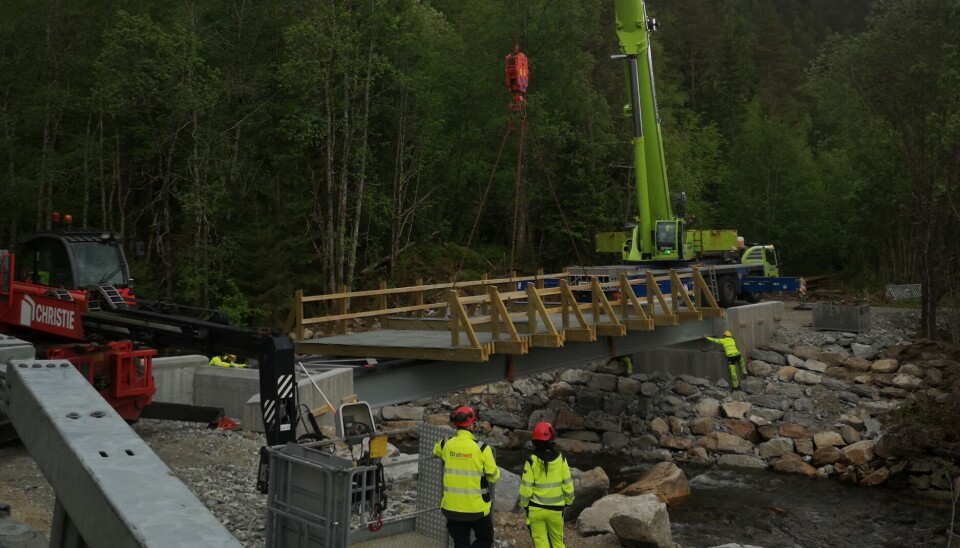 Dei siste finjusteringane, og brua er på plass. Kran, bru, elv og arbeidarar.