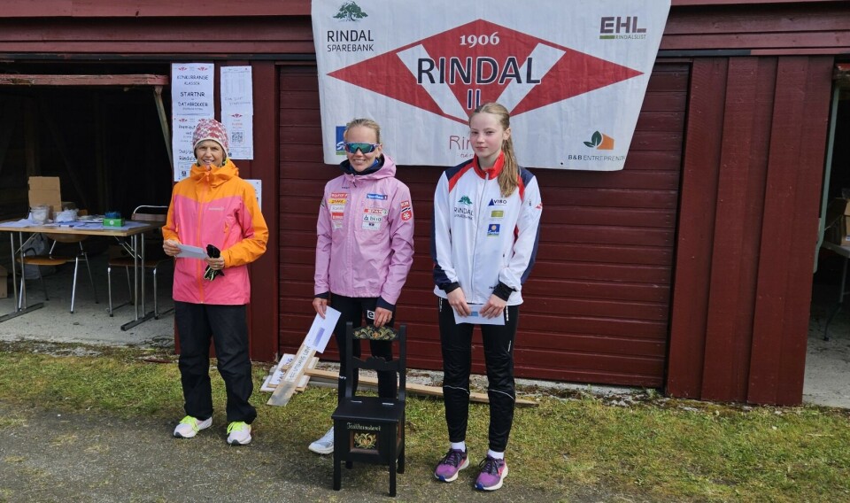 Berit Mogstad, Trollheimen Fjellsportsklubb, (i midten) vant dameklassen, og også vandrepremien i Trollheimsløpet mandag. Her sammen med de to med de nest beste tidene i dameklassen, Ann Kristin Amundsen, IL Norodd, etterfulgt av Anna Børset, Rindal IL (til høyre). Tre dameløpere foran garasje med idrettslags plakat. En med en rosemalt stol.