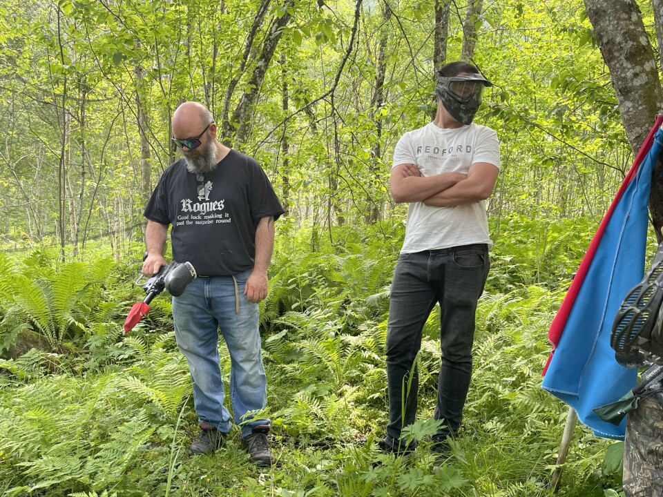 Terje Ranes (til venstre) og sønnen Råg Ranes forklarer sikkerhetsprosedyrer og hvordan våpen skal håndteres. To menn i skogen, den ene har et paintballgevær i hånden, den andre har på maske