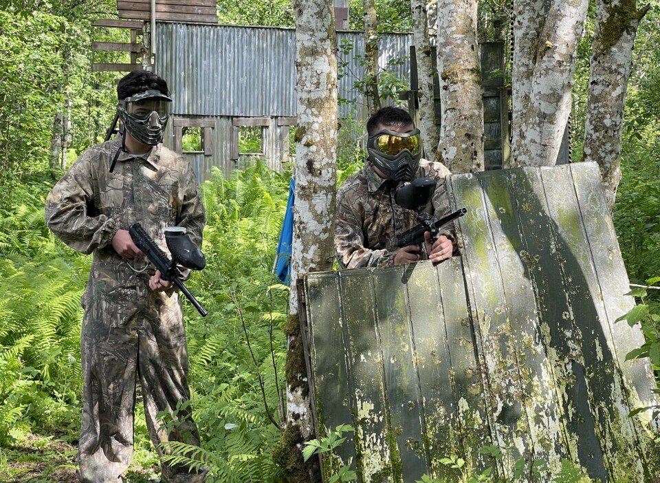 Her er guttene klare til en omgang med paintball To menn står med hvert sitt gevær. Den ene står bak en grønn vegg. De er i skogen