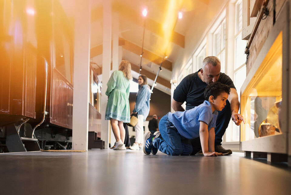 Ordfører i konduktørlue åpner utstilling på Orkla Industrimuseum Voksen og barn som er på en museumsutstilling.