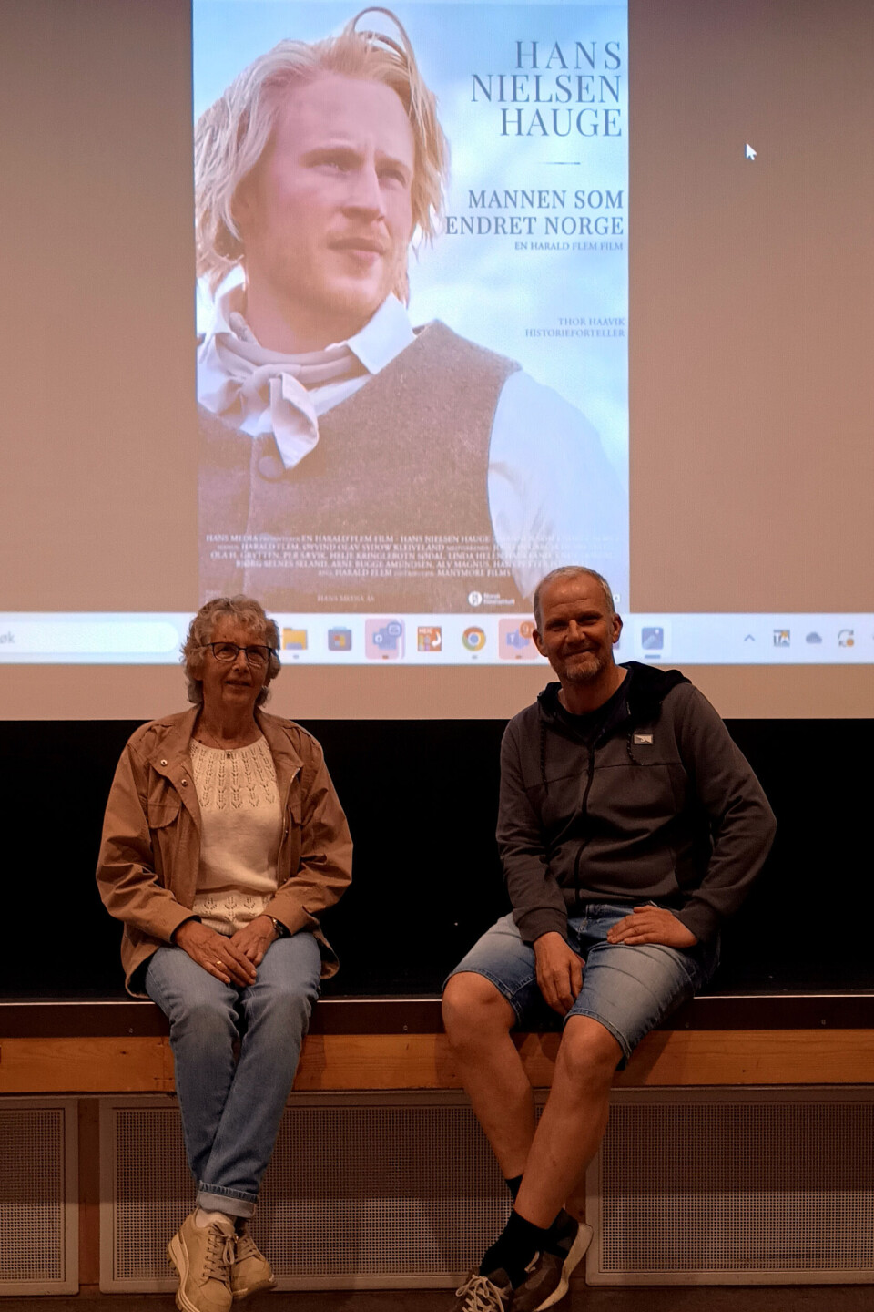 Kjellaug Foseide fra arrangementsgruppa Rindal sokn og Morten Møller, Rindal kino. Dame og mann på benk foran skjerm med kinoplakat