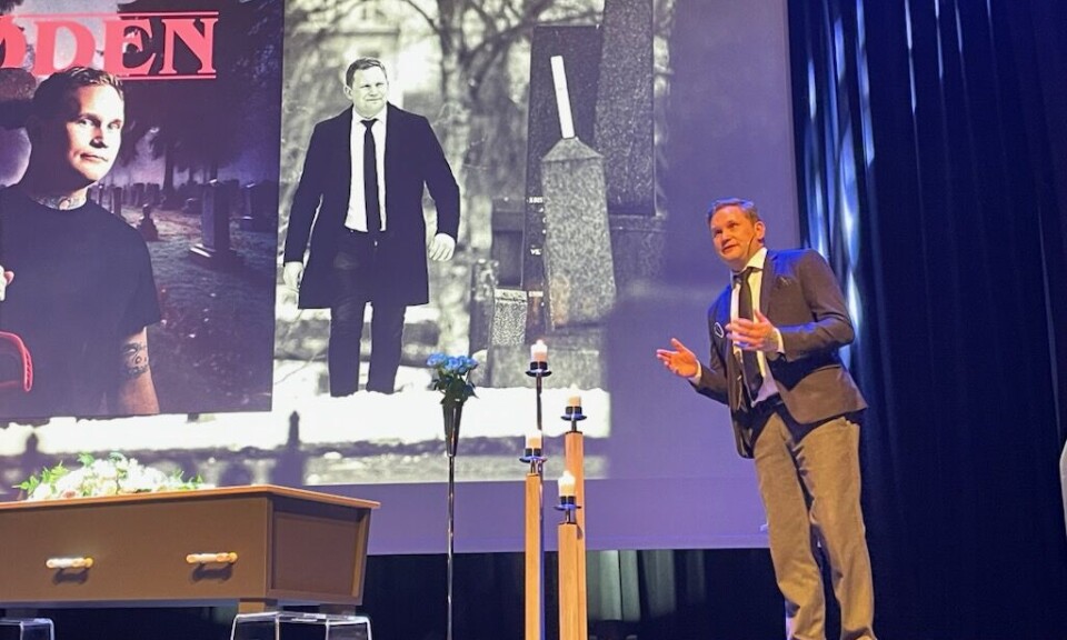 Tor-Håkon Garbiel Håvardsen engasjerte publikum i Storstuå med sin gode formidlingsevne En mann på en scene i dress. Levende lys og en kiste til venstre. BIlder på storskjerm i bakgrunnen