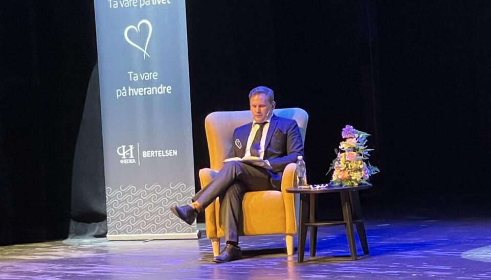 Her leser Edvardsen dikt. En mann sitter i en gul stol. til høyre for seg er det en likkiste