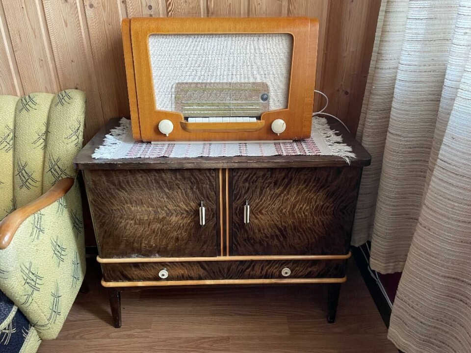 Denne radioen som står i leiligheten, er fra pauserommet på butikken på Nybø. Den kostet 580 kroner på 50-tallet. –Den ble aldri solgt. Jeg kom i eie av den av en bekjent, sier Kvande. Gammel radio på et gammelt skap ved en gammel sofa.