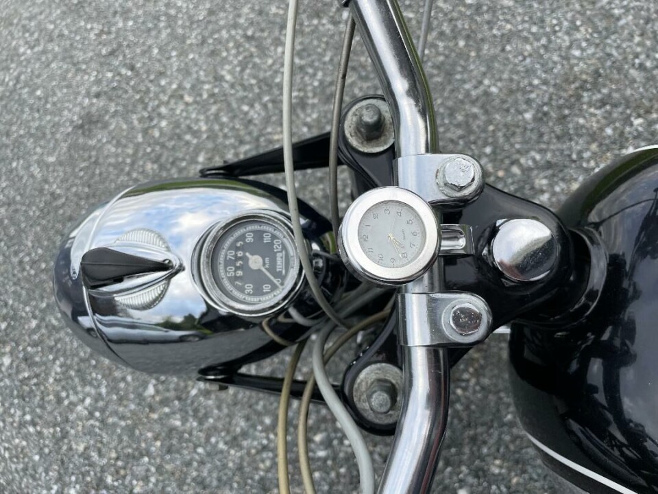 Detaljer. Det er montert en analog klokke på motorsykkelen. Litt av styret på en motorsykkel.