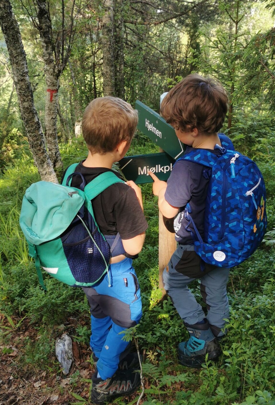 Førskolebarna på tur til Hjelmen To små gutter med sekk på ryggen, som leser på ent turskilt.