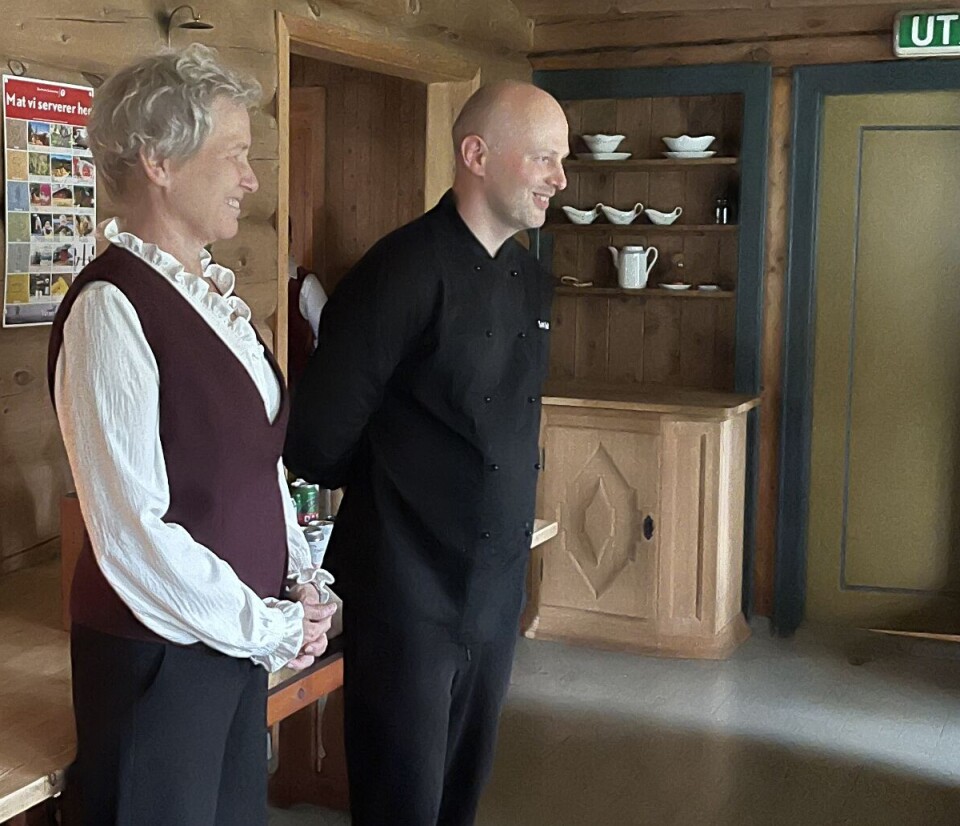 Førnøyde gjester takker kokken Lukaz og vertinne Hege. Ei dame og en mann i et rom med tømmervegger.