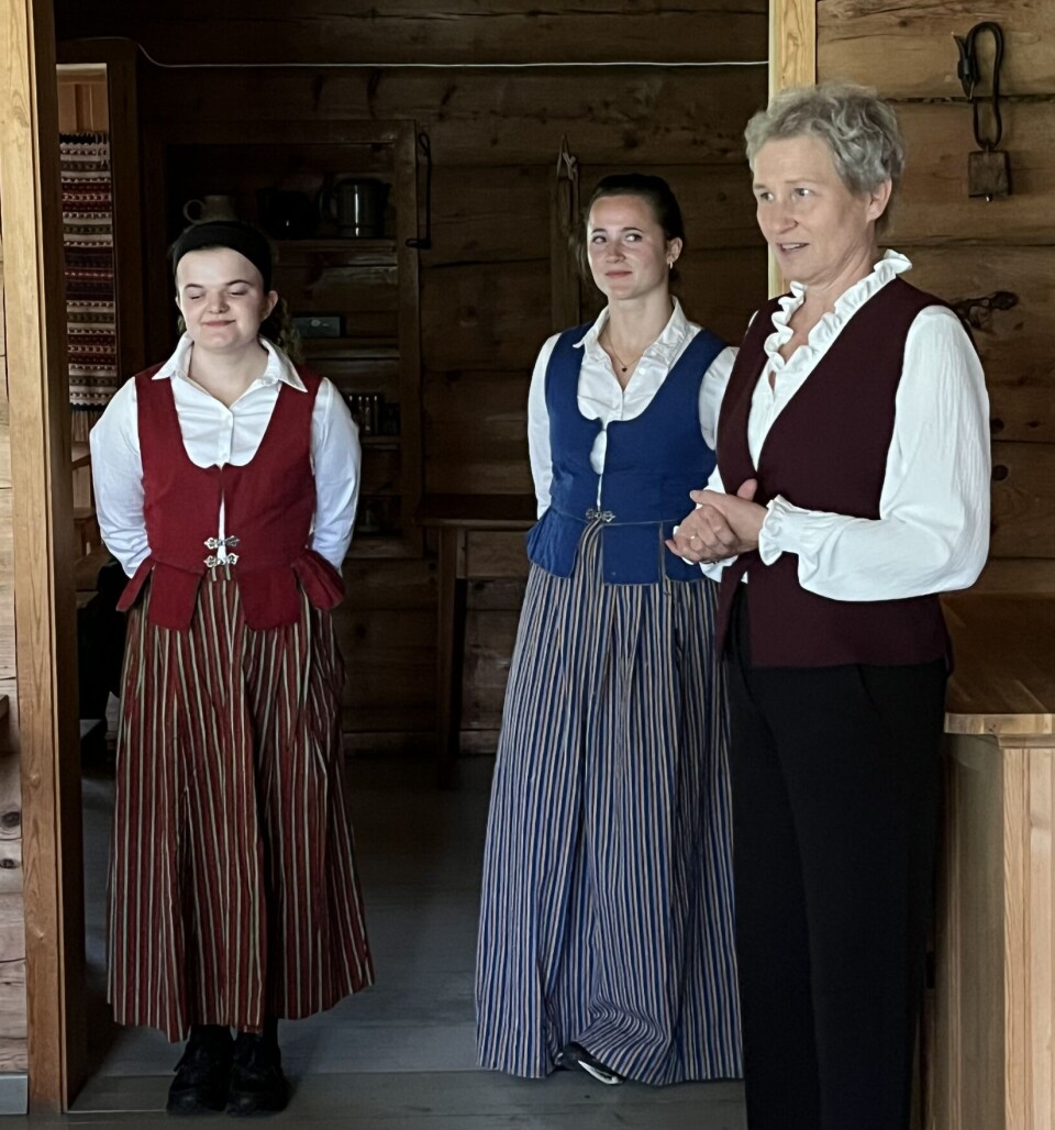 Hege og 'jentene' Oda og Rikke ønsker velkommen åpningskvelden, som andre kvelder inneholder informasjon om hytta og kveldens meny. Tre damer foran en tømmervegg.