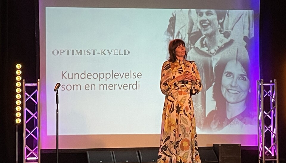 Bente Krangnes Edvardsen forteller om eget engasjement. Bildet i bakgrunnen er av Bente og hennes mor Ella EN dame med sid kjole på scena foran en skjerm. Bilde på skjermen er av to damer i svart hvitt