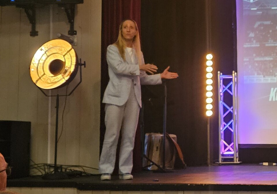 Cecilie Gotaas Johsen presentere RBK En kvinne på venstre side i bildet i grå dress. Står på en scene. Skjerm i bakgrunnen, med bilde av en mann på en fotballarena