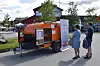 Tre personer som står og ser på ei lita campingvogn som er utstilt.