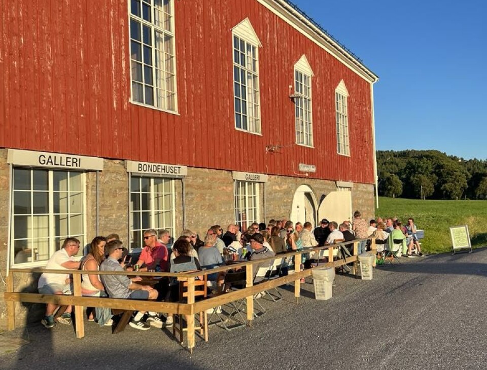 Mange mennesker som sitter ute foran et forsamlingshus på en fin sommerdag/kveld.