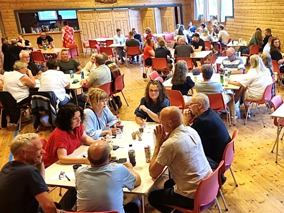 Quiz i grendahuset. Vinnarlaget sit nærast på bildet. Et forsamlingslokale der folk sitter rundt småbord.
