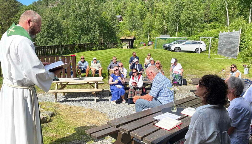 Frå ei tidlegare gudsteneste på Grendaplassen. Prost Vidar Rygh til venstre. prest leser foran folk på benker ute