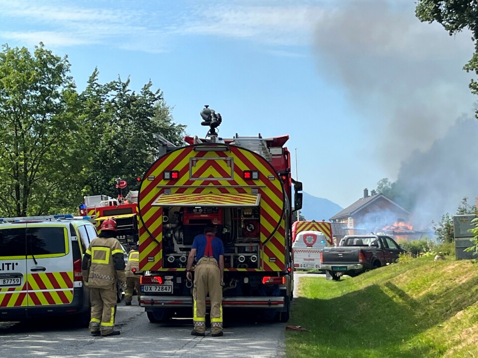 Alle nødetatene rykket ut. Brannbiler og en politibil ved en bygning som brenner. Sommer og solskinn, en del røyk.