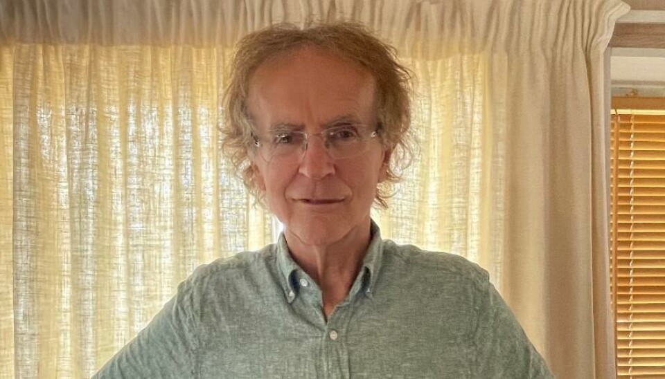 Henning Sommerro Bilde av en mann fra livet og opp. Mannen har bølgete hår og briller, og holder hendene inntil siden med albuene ut fra kroppen. Han har en grønn skjorte med knapper på seg.