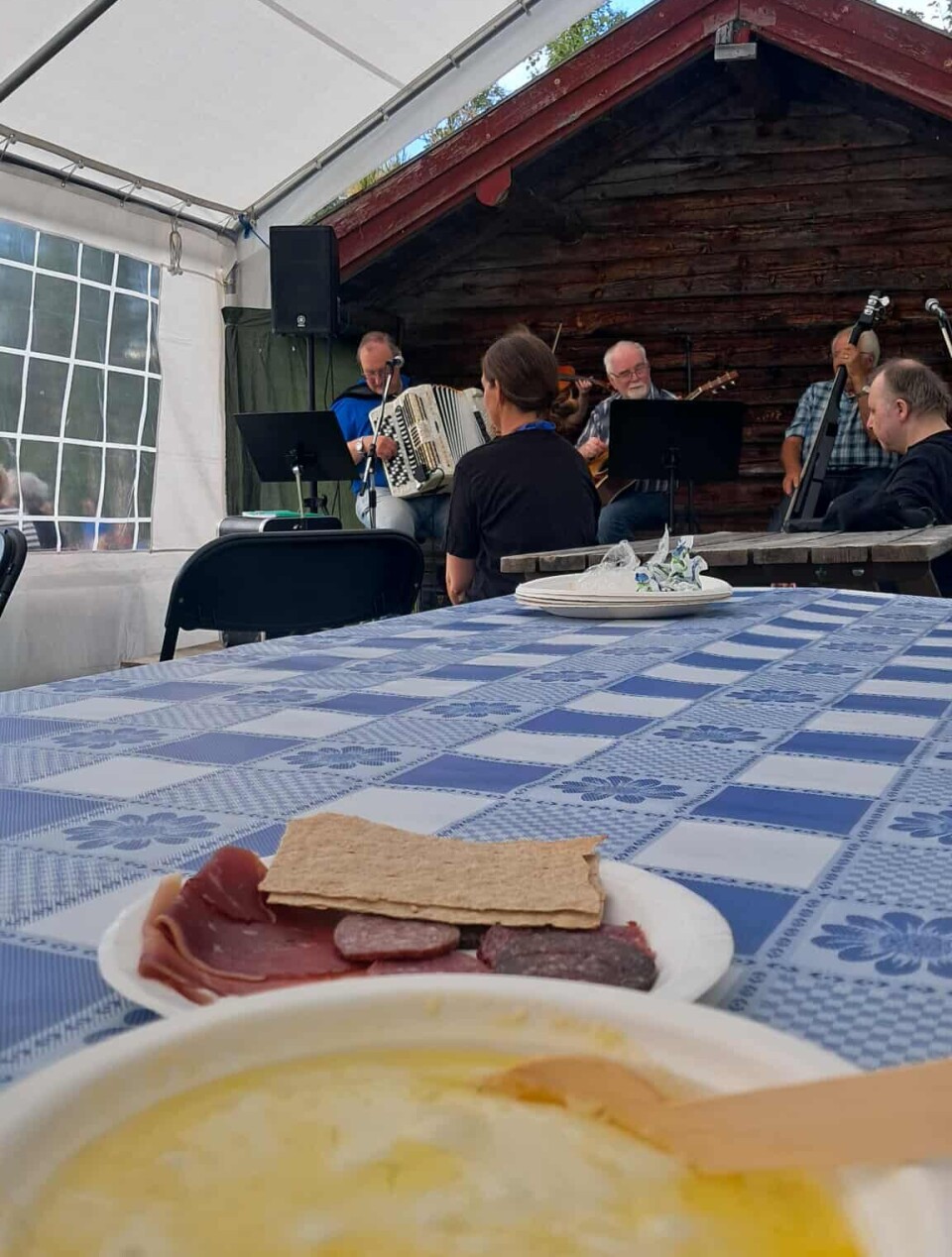 Rømmegrøt, spekemat og 'live' underholdning Bilde av rømmegrøt og spekemat på et bord, og et band med trekkspill, fiolin, gitar og bass i bakgruinnen