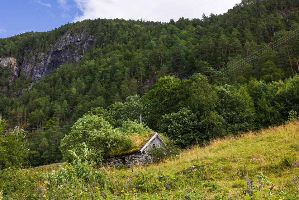 Gammelt kjølehus for isblokker Bilde av et gammelt hus med et berg i bakgrunnen