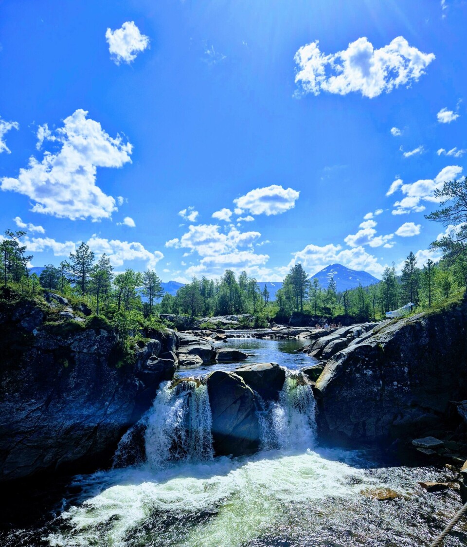En solskinnsdag i vakre Vindøldalen. Himmel, skog og elv med foss
