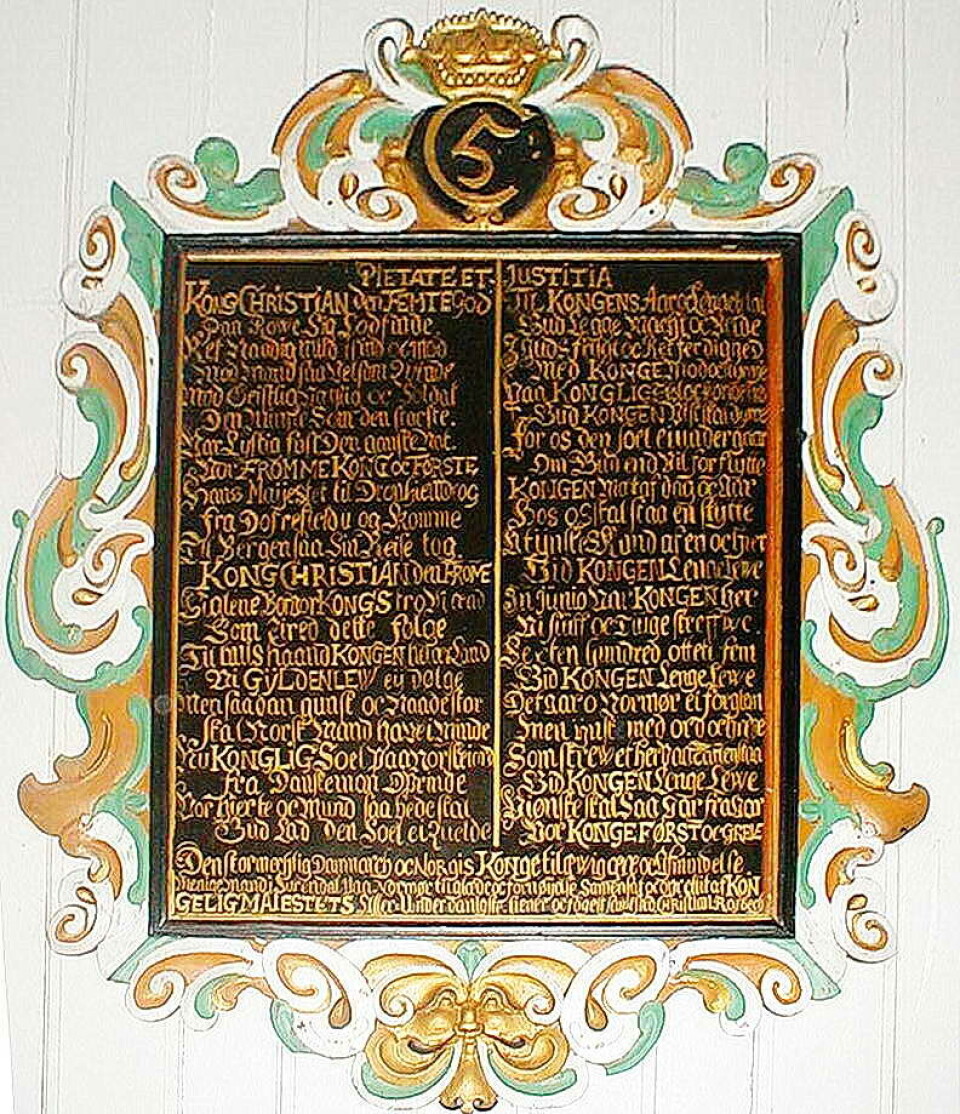 Kongetavla i Mo kyrkje – med Christian V sitt monogram og fogd Rasbech sitt dikt om kongebesøket i 1685. Ei veggtavle med gammel skrift og utsmykninger rundt. En konges monogram på toppen.