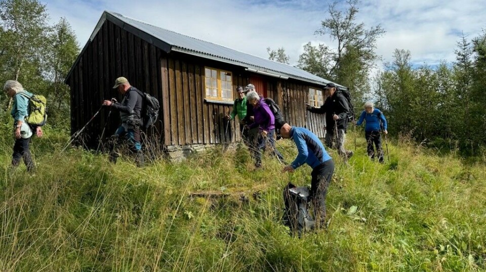 Holmvassetra. Flere turkledde personer ved et seterhus på fjellet, i sommervær. Skyer på himmelen.