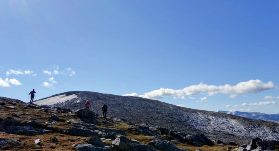 Rindhatten. Tre personer skimtes i forkant av en avrundet fjelltopp, og blå himmel bak-