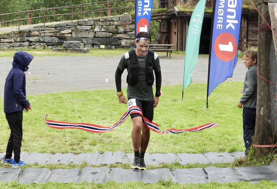 Erik Kårvatn var først i mål i skyrace på hjemmebane. En smilende ung mørkhåret mann i treningsklær, og med startnummer, som passerer en målstrek. Sommer og regnvær.