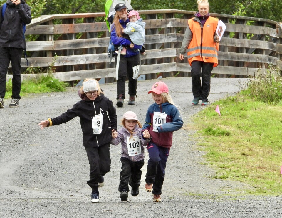 Erik Kårvatn med ny løyperekord i Kårvatn skyrace Seks smilende barn og voksne som går/småløper på en grusvei med startnummer på brystet. I forgrunnen to jenter som holder ei mindre jente mellom se og småløper. Grått sommervær.