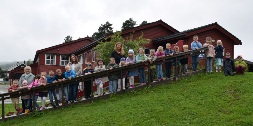Første skoledag på Rindal skole 23 førsteklassinger og tre lærere oppstilt i ei utendørs trapp, men skolebygget i bakgrunnen. Grått sommervær.
