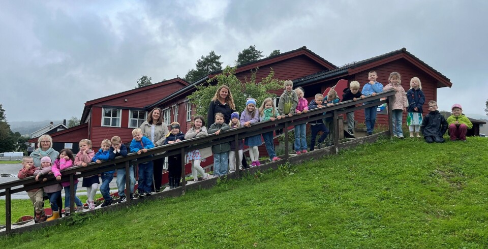Første skoledag på Rindal skole 23 førsteklassinger og tre lærere oppstilt i ei utendørs trapp, men skolebygget i bakgrunnen. Grått sommervær.