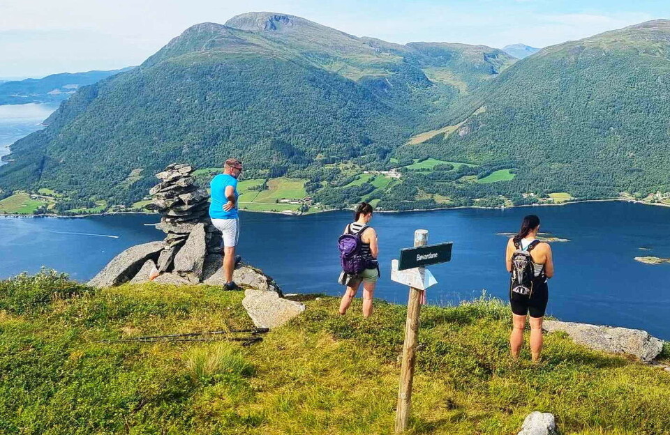 Praktfull utsikt frå Bølia – over Bøfjorden mot Kristiansund og Trøndelag. Tre turkledde personer ved en varde på en høyde, med utsikt over fjord og fjell. Sommer og sol.