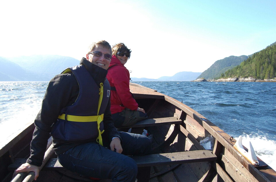 Båttur langs Kalsetlandet i frisk sommarbris. To smilende personer i en trebåt på fjorden i sommervær.
