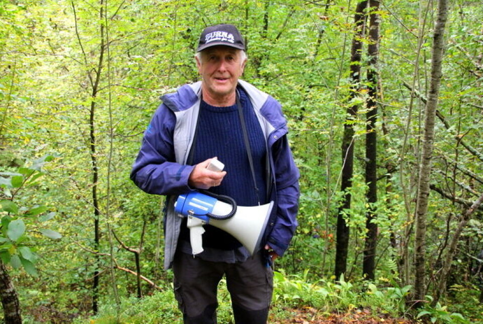 Øyvind Holte inviterer til forsvarshistorisk vandring på Øye - denne gangen heldigitalt. Her fra vandringen i 2019 Mann med caps, blå jakke og megafon stående i skogen