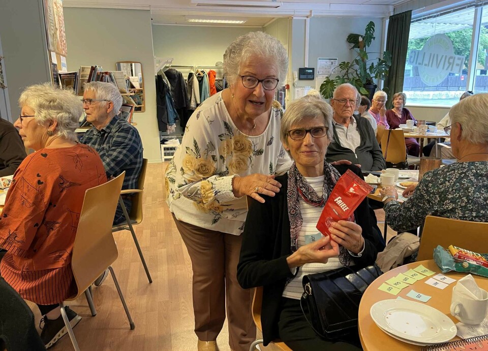 Utlodning høyrer med. Ein heldig vinnar var Kari Marie Sæter (t.h.). Herdis Solli delte ut gevinstar. Ei dame med kort grått hår og briller som sitter et rom med flere godt voksne personer rundt små bord. Hun holder en liten kaffepose i hendene. Ei dame med kort krøllet grått hår og briller står bak henne og holder en hånd på skulderen hennes.