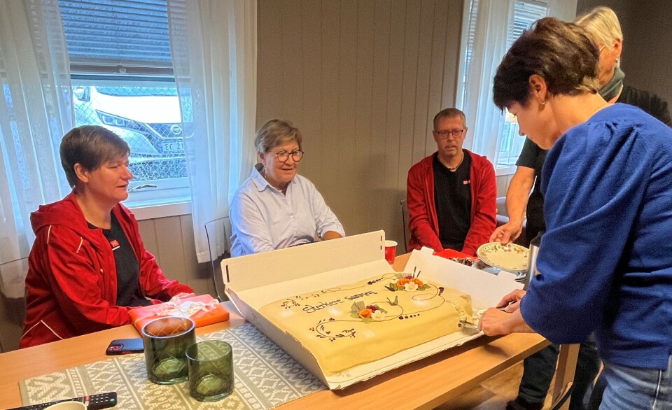 Fagforbundet spanderte bløtkake. Enhetsleder Signe Lill Aasland skjærer opp kaken. På andre siden av bordet sitter Fagforbundets nestleder Helene Harsvik Skeibrok, leder Mette Nord og Geir Ole Kanestrøm, som er leder i Fagforbundet Møre og Romsdal. Ei dame som skjærer et stykke av ei stor bløtkake. Flere personer sitter rundt bordet.