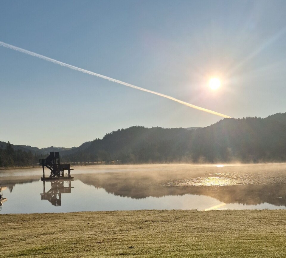 Morgenbilde fra Tjønna. Morgendis i sola over blikkstille vann og blå himmel