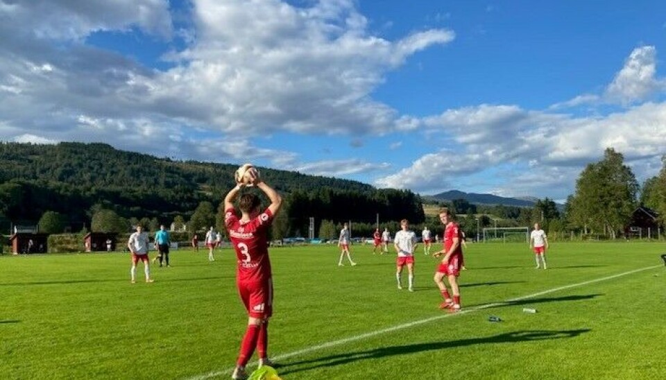 Friskt topp-oppgjer fotballspillere med røde drakter, en holder ballen over hodet