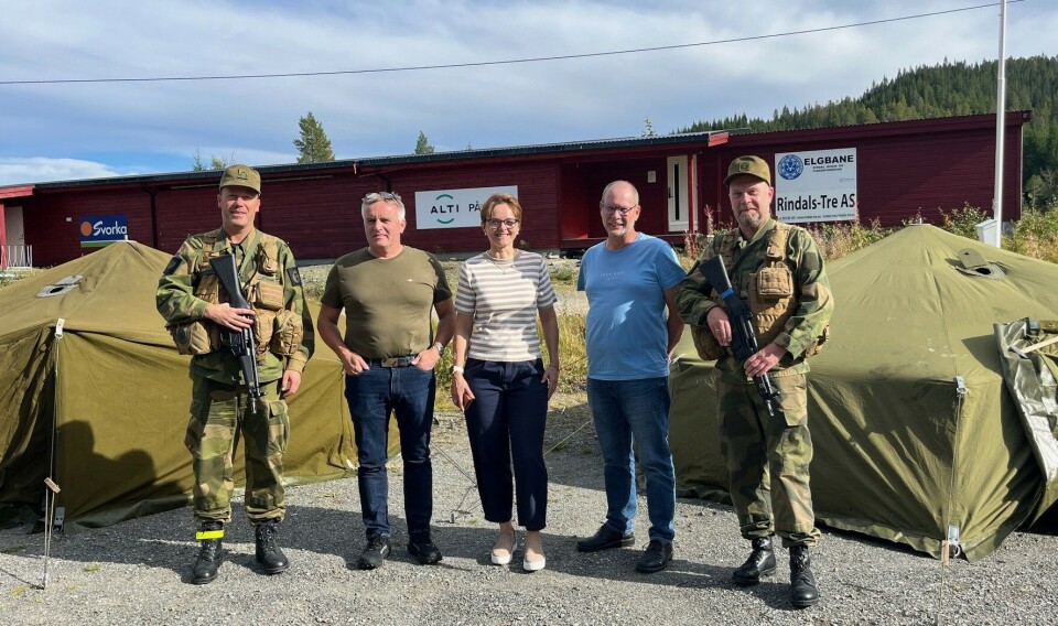 F.v. etterretningsoffiser/løytnant Kristian Kvam Lønnum, beredskapsansvarlig i Rindal kommune Kåre Herrem, ordfører Mildrid Kattem Aune, kommunedirektør Mons Otnes og liaisonoffiser John Arnold Merkesnes. To soldater i uniform, og ei dame og to menn i sivil som står mellom dem. To militære åttemannstelt i bakgrunnen. Sommer og solskinn.