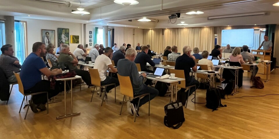 Slit framleis med meirforbruk Flere personer som sitter ved små bord i et møterom.