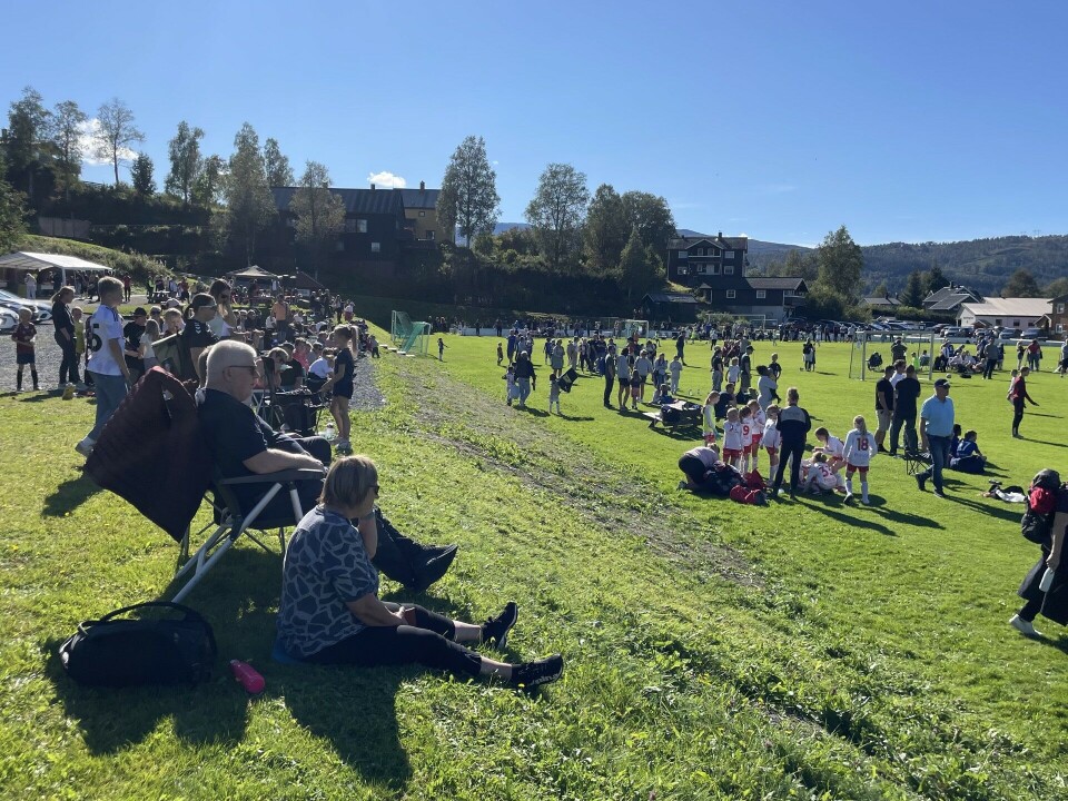 Mye publikum hadde funnet veien til Trollbanen på søndag Oversiktsbilde over plassen. Vi ser barn som spiller fotball. Mange mennesker sitter i en skråning og på en tribune, mens noen står på banen.