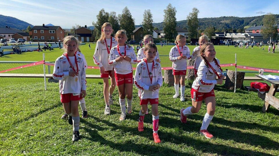 Rindalscup i strålende vær Åtte jenter i hvite og røde Rindal IL drakter som løper og går fra oppstillingen med medaljer rundt halsen.