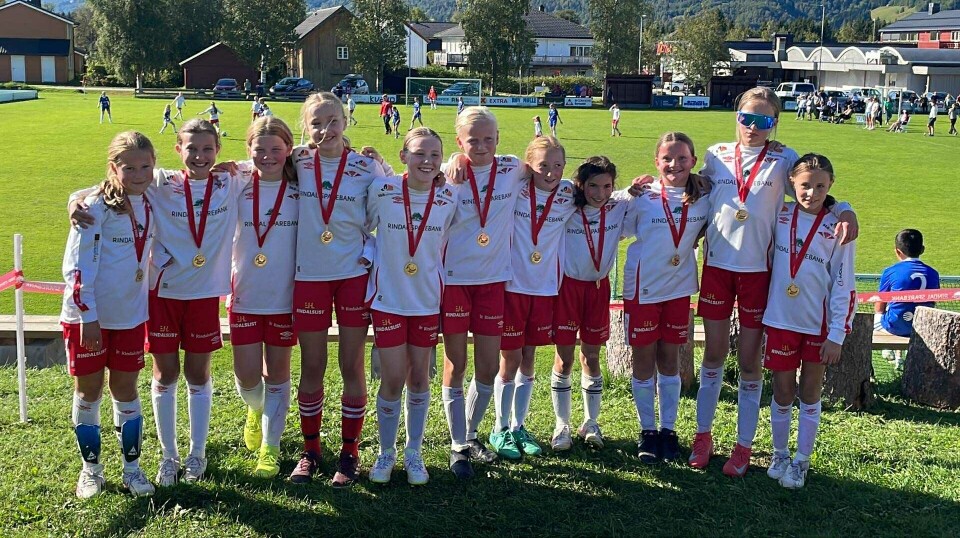 Rindalscup i strålende vær Elleve jenter i røde og hvile Rindal IL drakter, smiler med medaljer rundt halsen.